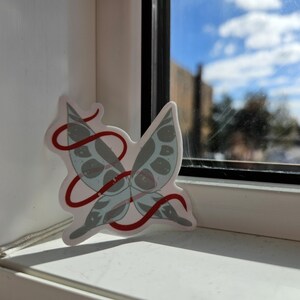 May include: A white butterfly sticker with red ribbon detail, on a white windowsill.