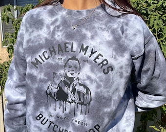 May include: A gray tie-dye sweatshirt with a black graphic of Michael Myers, the character from the Halloween movies. The graphic includes the text "Michael Myers Est. 1978 Always Fresh Butcher Shop".