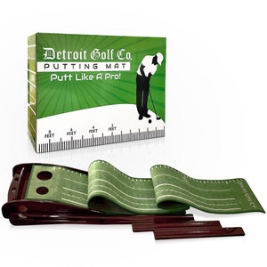 May include: A green putting mat with white lines and a brown wooden base. The box reads "Detroit Golf Co. PUTTING MAT Putt Like A Pro!" with a graphic of a golfer. The mat has measurements in feet.