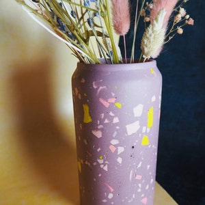 May include: A purple terrazzo vase with pink and yellow flecks, filled with dried flowers, including lavender and bunny tail grass.