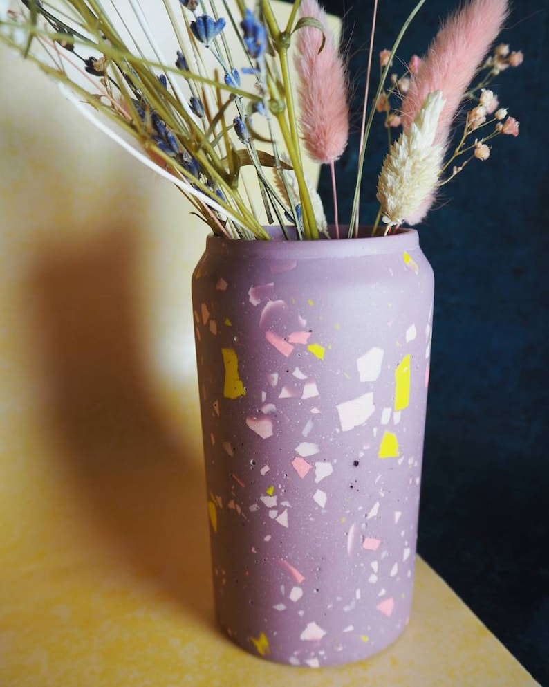 May include: A purple terrazzo vase with pink and yellow flecks, filled with dried flowers, including lavender and bunny tail grass.