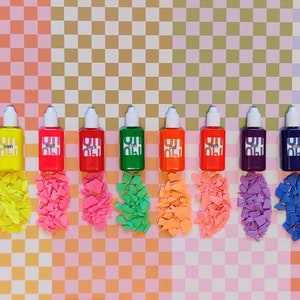 May include: Ten small bottles of colorful liquid paint arranged in a row on a checkered background. The bottles are labeled with the words "Chill", "Sunny", "Wight", "Yello", "Ultra", "Star", "Astro", "Strobe", "Iture", and "Future".