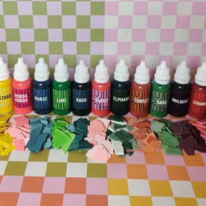 May include: A set of 16 small bottles of paint with labels for each color. The colors include toffee, tephra, mustard, hubba hubba, norse, lime, aqua, blush, elphaba, sunset, sage, mulberry, strawberry, seafoam, and peach keen.