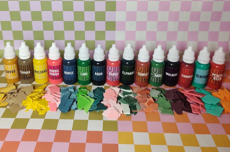 May include: A set of 16 small bottles of paint with labels for each color. The colors include toffee, tephra, mustard, hubba hubba, norse, lime, aqua, blush, elphaba, sunset, sage, mulberry, strawberry, seafoam, and peach keen.