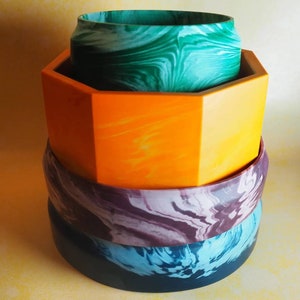 Op de afbeelding: Een stapel van vier kleurrijke kommen met marmerpatronen. De bovenste kom is groen, de tweede is oranje, de derde is paars en de onderste is blauw.