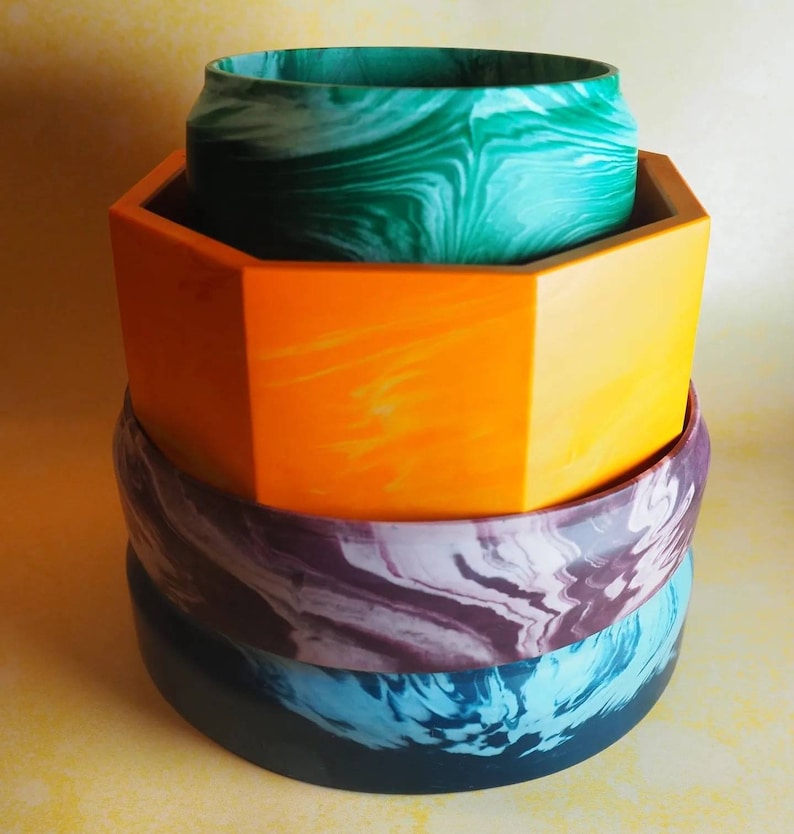 Op de afbeelding: Een stapel van vier kleurrijke kommen met marmerpatronen. De bovenste kom is groen, de tweede is oranje, de derde is paars en de onderste is blauw.