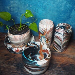 May include: Four colorful, swirl-patterned ceramic planters, one with a green plant inside. The planters are on a wooden surface.