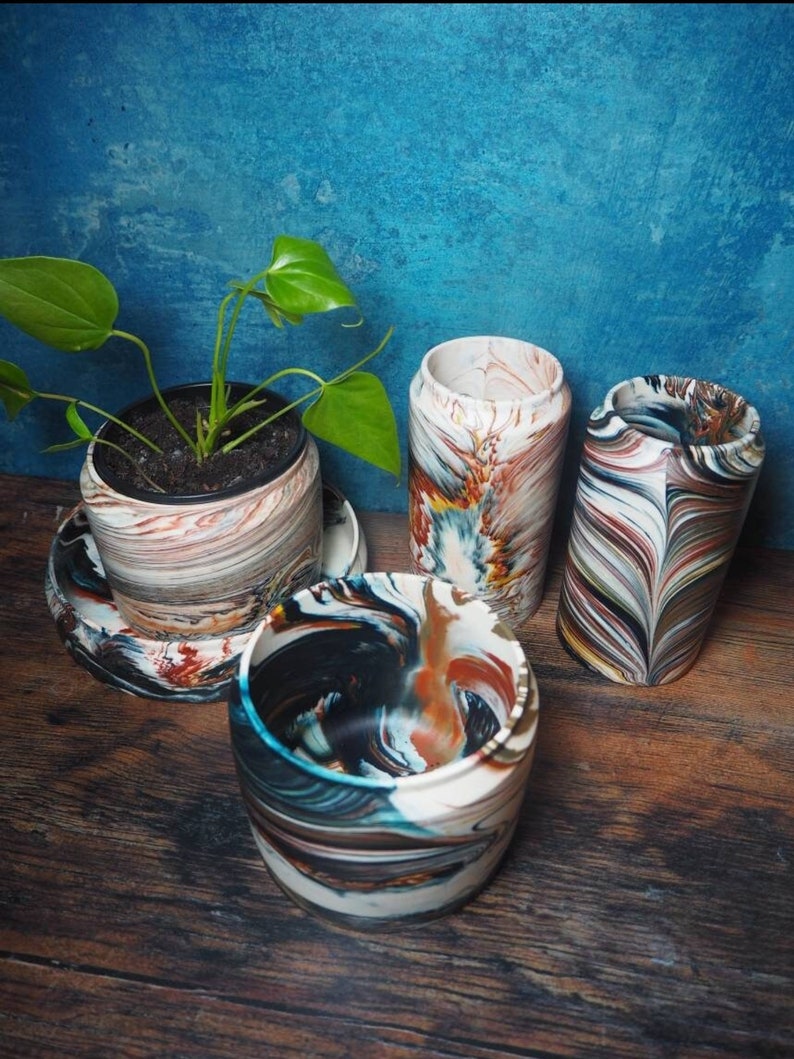 May include: Four colorful, swirl-patterned ceramic planters, one with a green plant inside. The planters are on a wooden surface.