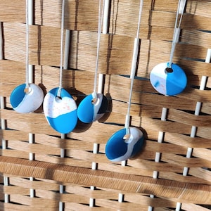 May include: Five necklaces with blue and white oval-shaped pendants. The pendants have a marbled effect with white and blue swirls. The necklaces are hanging on a woven wicker background.