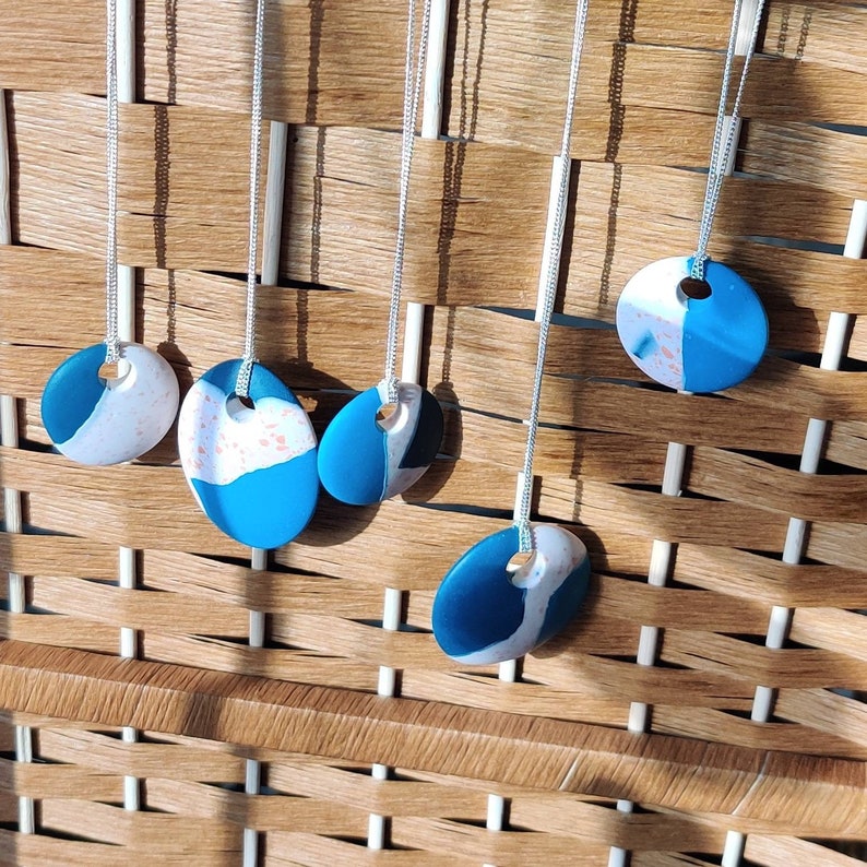 May include: Five necklaces with blue and white oval-shaped pendants. The pendants have a marbled effect with white and blue swirls. The necklaces are hanging on a woven wicker background.