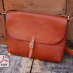Puede incluir: Un bolso de mensajero de cuero marrón con cierre de solapa y hebilla de latón. El bolso tiene una correa larga ajustable.