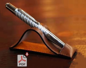 May include: A brown leather pen holder with a silver and white pen resting inside. The pen holder is shaped like a curved stand.