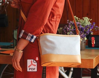 Op de afbeelding: Een lichtblauwe canvas tote bag met een bruine leren afwerking en een lange bruine leren band. De tas wordt gedragen door iemand die een rood jack draagt.