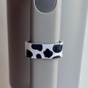 May include: A gray travel mug with a black and white cow print handle wrap.