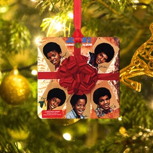 May include: A square Christmas ornament featuring a red bow and a vintage album cover of the Jackson 5's Christmas album. The album cover features the five brothers, with their names written below their images. The text on the album cover reads "Jackson 5 Christmas Album".