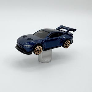 May include: A dark blue toy car with a black roof and gold-coloured wheels. The car has a spoiler and is elevated on a silver stand. The car is a miniature replica of a sports car.