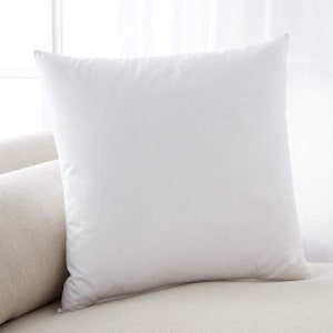 May include: A white pillow with a smooth, soft surface. The pillow is lying on a light beige sofa.