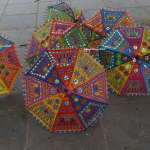 May include: A collection of colourful, hand-stitched umbrellas with intricate designs featuring elephants, flowers, and mirror accents. The umbrellas are made of fabric and have a traditional Indian style.