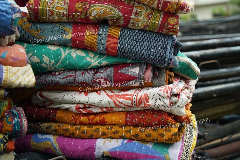 Puede incluir: Una pila de colchas kantha coloridas con intrincados patrones y costuras. Las colchas est&aacute;n hechas de saris reciclados y son una artesan&iacute;a tradicional india. Copyright@VillageWomenSkill