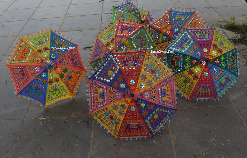 May include: A collection of colourful, hand-stitched umbrellas with intricate designs featuring elephants, flowers, and mirror accents. The umbrellas are made of fabric and have a traditional Indian style.