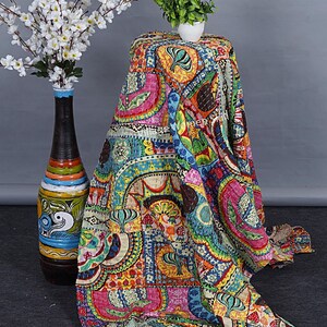 Puede incluir: Una colcha kantha colorida con un dise&ntilde;o de patchwork que presenta varias formas geom&eacute;tricas, patrones florales y motivos paisley. La colcha est&aacute; hecha de algod&oacute;n y tiene un aspecto cosido a mano. Est&aacute; drapeada sobre una mesa con una peque&ntilde;a planta en maceta en la parte superior.