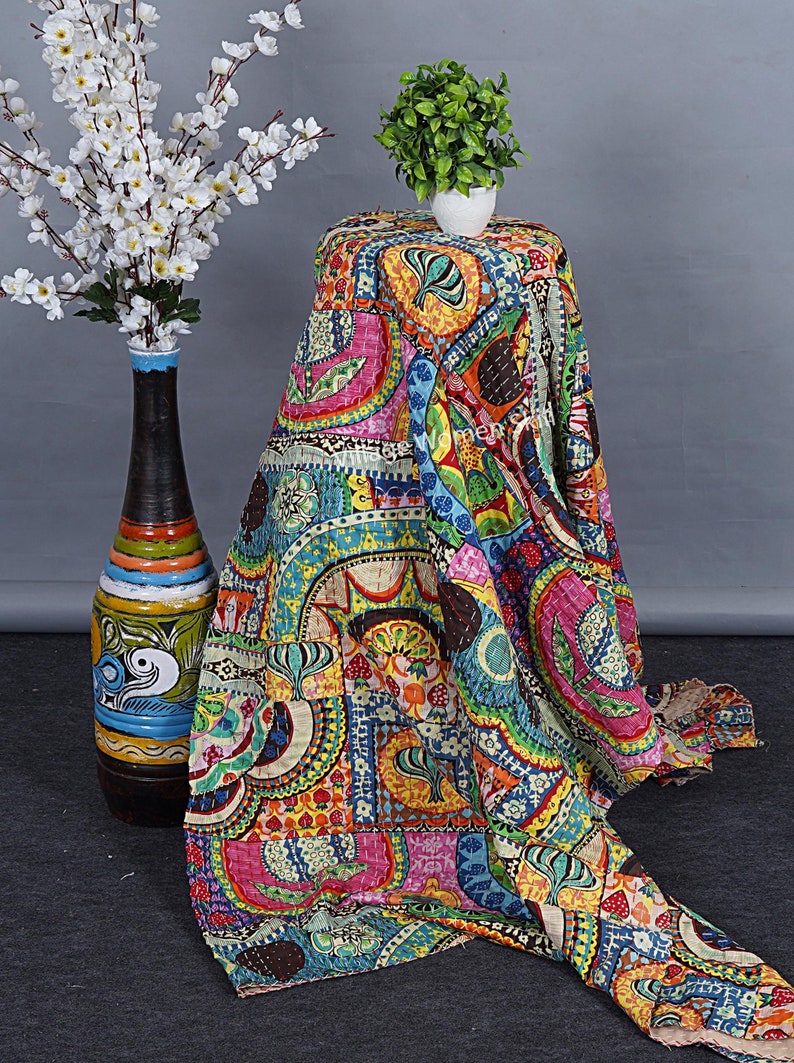 Puede incluir: Una colcha kantha colorida con un dise&ntilde;o de patchwork que presenta varias formas geom&eacute;tricas, patrones florales y motivos paisley. La colcha est&aacute; hecha de algod&oacute;n y tiene un aspecto cosido a mano. Est&aacute; drapeada sobre una mesa con una peque&ntilde;a planta en maceta en la parte superior.