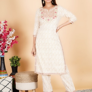 May include: White cotton kurta and palazzo set with gold and pink embroidery. The kurta has a V-neckline and three-quarter sleeves. The palazzo pants have a wide leg.