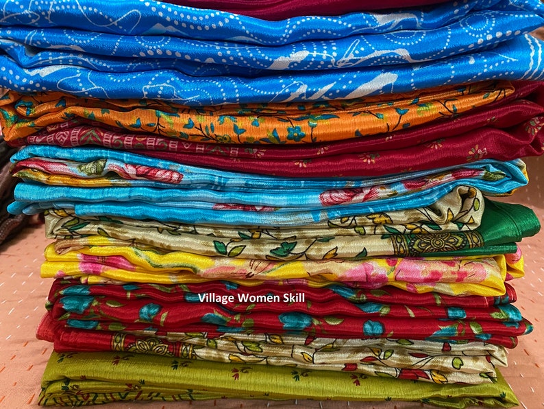 May include: A stack of colorful fabric scarves with floral and geometric patterns. The scarves are folded neatly and arranged in a pile. The text "Village Women Skill" is visible on the bottom of the pile.