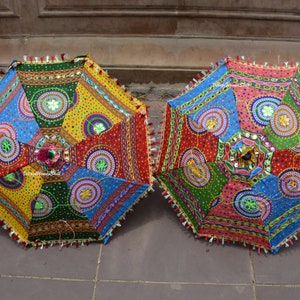 Puede incluir: Dos paraguas redondos de tela coloridos con bordados intrincados y adornos de espejo. Los paraguas est&aacute;n cerrados y presentan una variedad de colores, incluyendo rojo, azul, verde, amarillo y rosa.