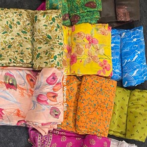 May include: A collection of colorful fabric squares with floral and geometric patterns. The fabrics are arranged in a pile on a gray surface. The text "Village Women Skill" is visible on one of the fabrics.