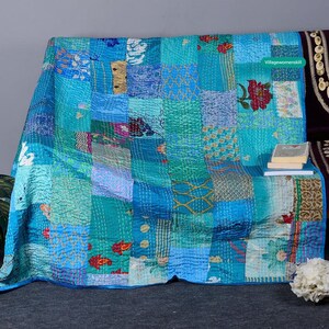 May include: A patchwork quilt with a blue and green color scheme. The quilt is made of various fabrics with different patterns and textures. The quilt is folded and displayed on a couch.