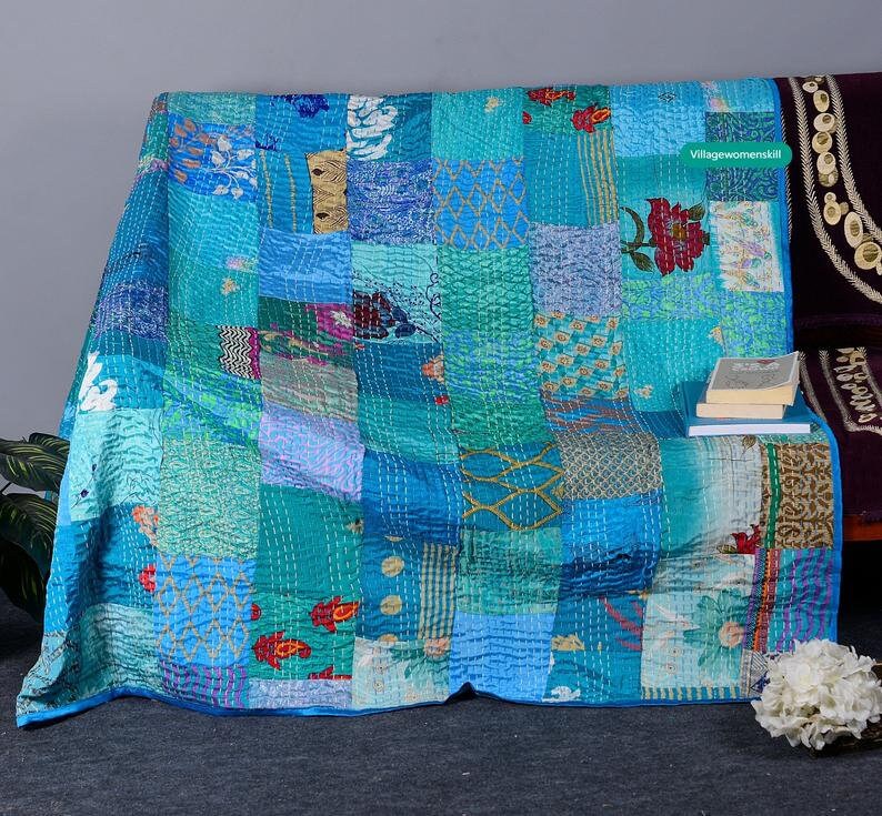 May include: A patchwork quilt with a blue and green color scheme. The quilt is made of various fabrics with different patterns and textures. The quilt is folded and displayed on a couch.