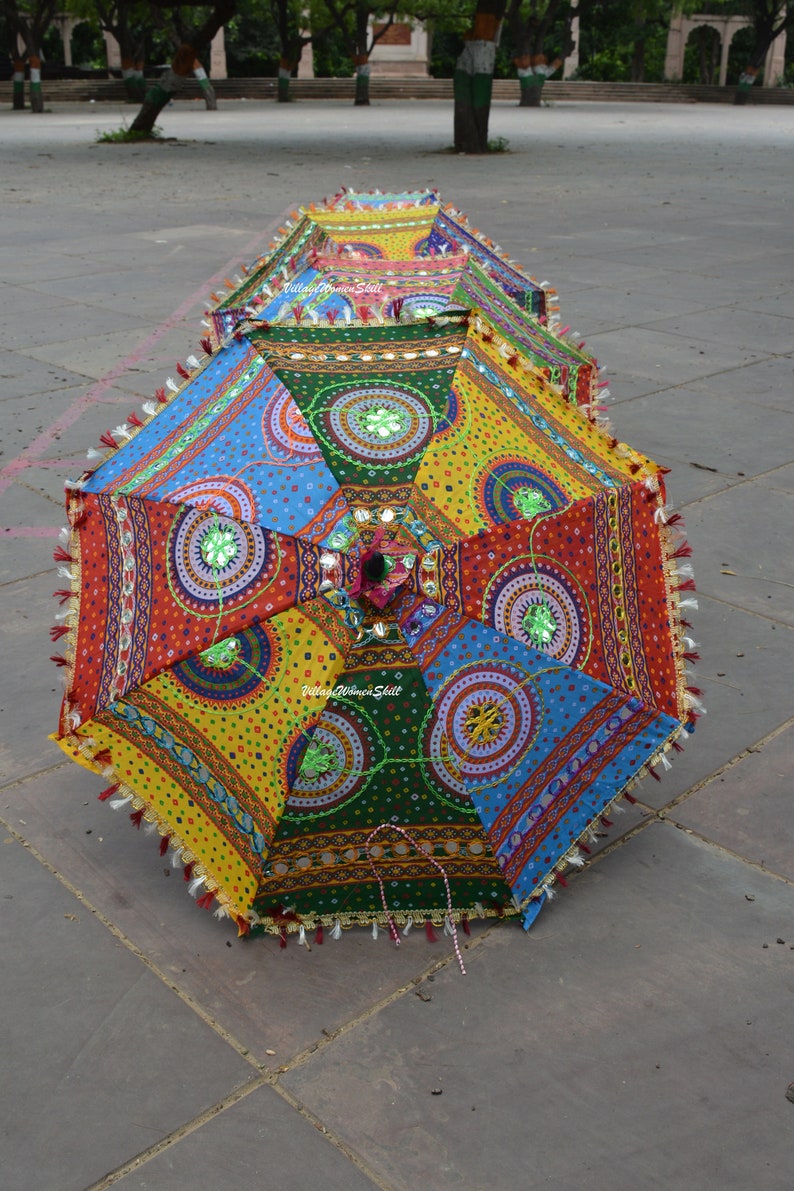 Puede incluir: Una sombrilla colorida y estampada con ribete de flecos. La sombrilla est&aacute; hecha de tela y tiene una variedad de colores, incluyendo rojo, amarillo, azul, verde y blanco. La sombrilla est&aacute; decorada con peque&ntilde;os espejos y cuentas.