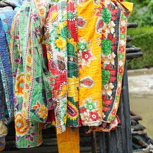 Puede incluir: Una pila de colchas kantha coloridas con motivos florales en tonos rojos, amarillos, verdes y azules. Las colchas est&aacute;n colgadas en un estante de madera.