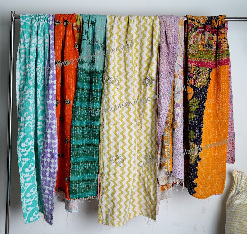 May include: Seven colorful kantha quilts hanging on a clothesline. The quilts are made of patchwork fabric and have a variety of patterns, including floral, geometric, and paisley. The quilts are all different sizes and shapes.