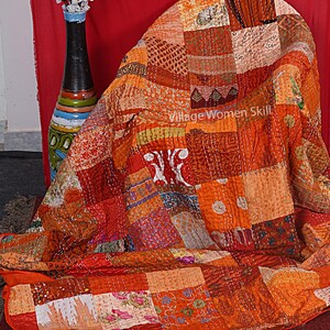 May include: A patchwork quilt made of various fabrics in shades of orange, red, and brown. The quilt is hand-stitched and has a unique, rustic look. "Village Women Skill" is written on the quilt.