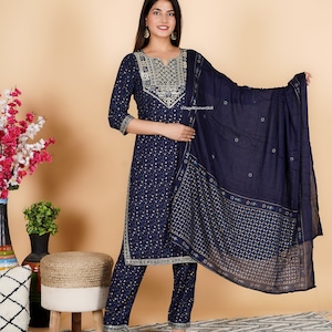 May include: A navy blue three-piece suit with gold embroidery. The suit includes a long-sleeved kurta, trousers, and a dupatta. The kurta has a V-neckline and a floral pattern. The trousers are straight-leg and the dupatta is sheer with a floral pattern. The text "Village Womenskill" is visible on the dupatta.