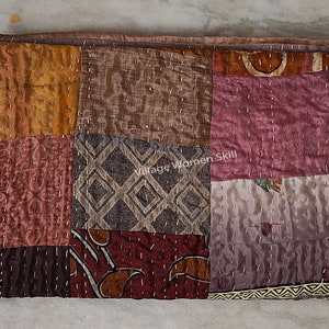 May include: A patchwork quilt made of various fabrics in shades of brown, pink, and orange. The quilt is hand-stitched with small, evenly spaced stitches. The quilt is folded in half and lying on a light-colored surface. The text "Village Women Skill" is visible in the center of the quilt.