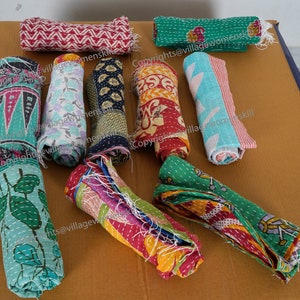 May include: A collection of colorful, rolled up kantha quilts with various patterns and designs. The quilts are made of recycled saris and are hand-stitched. The quilts are a traditional Indian craft and are known for their durability and beauty.