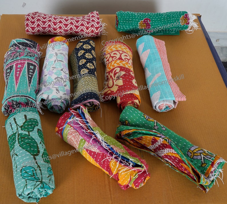 May include: A collection of colorful, rolled up kantha quilts with various patterns and designs. The quilts are made of recycled saris and are hand-stitched. The quilts are a traditional Indian craft and are known for their durability and beauty.