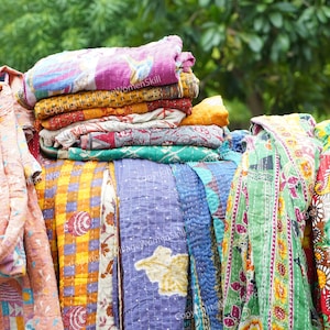 May include: A stack of colorful kantha quilts with floral and geometric patterns. The quilts are made from recycled saris and are a traditional Indian craft.