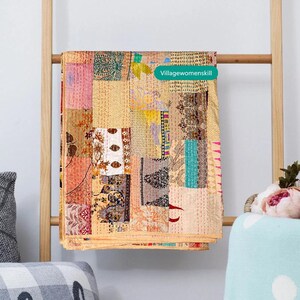 May include: A multi-colored patchwork quilt with a variety of patterns and textures. The quilt is made of recycled saris and is hand-stitched. The quilt is hanging on a wooden ladder. The text "Villagewomenskill" is visible in the upper right corner of the image.