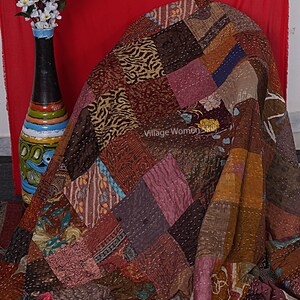 May include: A patchwork quilt made from various fabrics in shades of brown, pink, and blue. The quilt is folded and draped over a chair. The text "Village Women Skill" is visible on the quilt.