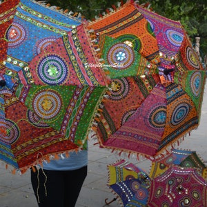 May include: Colorful, patterned umbrellas with intricate designs and embellishments. The umbrellas feature a variety of colors, including red, blue, orange, and green, with decorative trim and tassels. The text "Village Women Skill" is visible on one of the umbrellas.