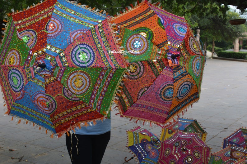 May include: Colorful, patterned umbrellas with intricate designs and embellishments. The umbrellas feature a variety of colors, including red, blue, orange, and green, with decorative trim and tassels. The text "Village Women Skill" is visible on one of the umbrellas.