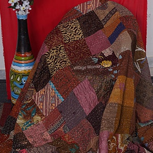 May include: A patchwork quilt made from various fabrics in shades of brown, pink, and blue. The quilt is folded and draped over a chair. The text "Village Women Skill" is visible on the quilt.