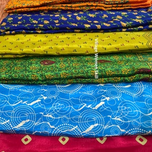 May include: A stack of six colorful fabric swatches with different patterns. The fabrics are arranged from top to bottom in the following order: red, orange, blue, green, light blue, and red. The fabrics are all patterned with small, geometric designs. The text "Village Women Skill" is visible on the green fabric.
