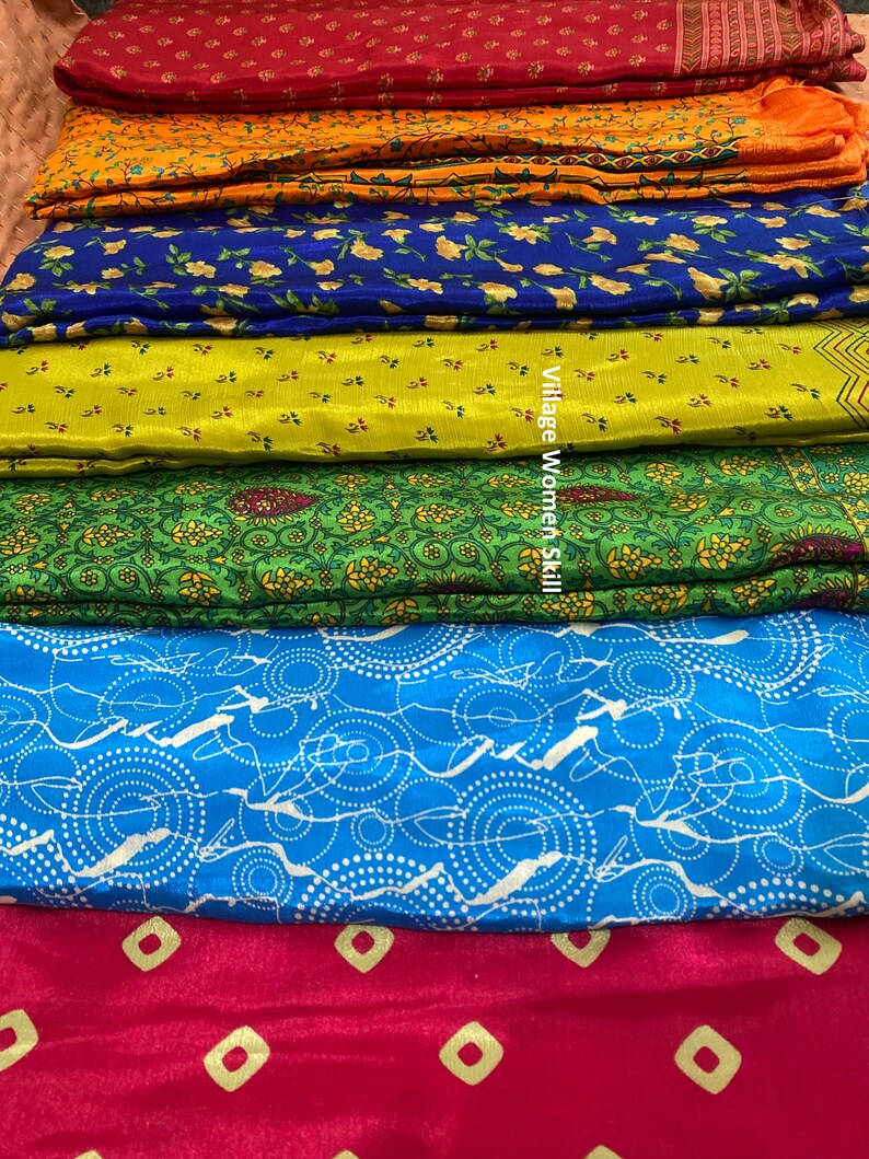 May include: A stack of six colorful fabric swatches with different patterns. The fabrics are arranged from top to bottom in the following order: red, orange, blue, green, light blue, and red. The fabrics are all patterned with small, geometric designs. The text "Village Women Skill" is visible on the green fabric.
