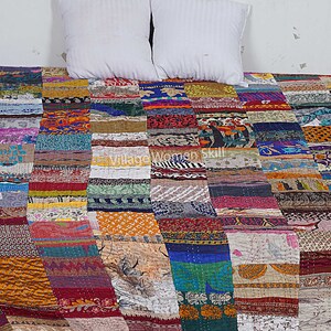 May include: A colorful patchwork quilt made from recycled saris. The quilt is made up of squares of different fabrics and colors, and is a beautiful example of Indian craftsmanship.