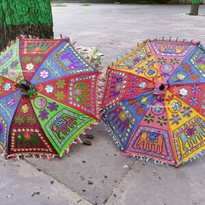 May include: Two colourful umbrellas with embroidered elephant designs and mirror accents. The umbrellas are made of fabric and have a fringe trim.